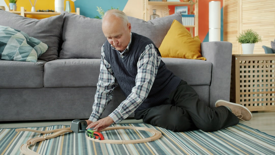 Elderly man playing with a wooden toy train set.