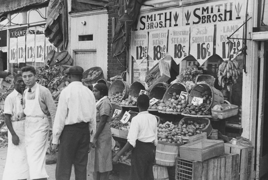 People shop at a produce stand with prices displayed.