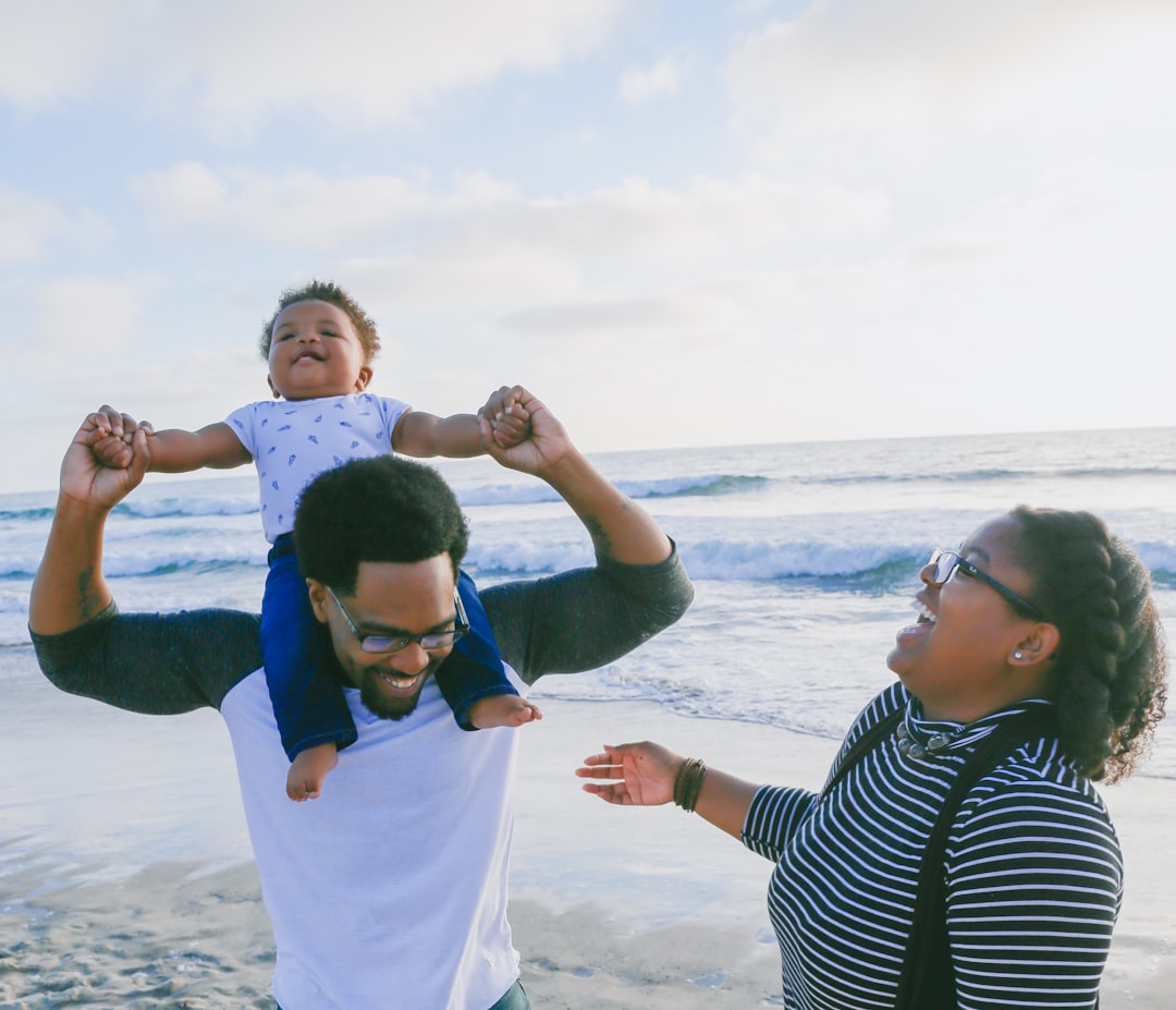 A family on a beach with a man carrying a baby on his shoulders